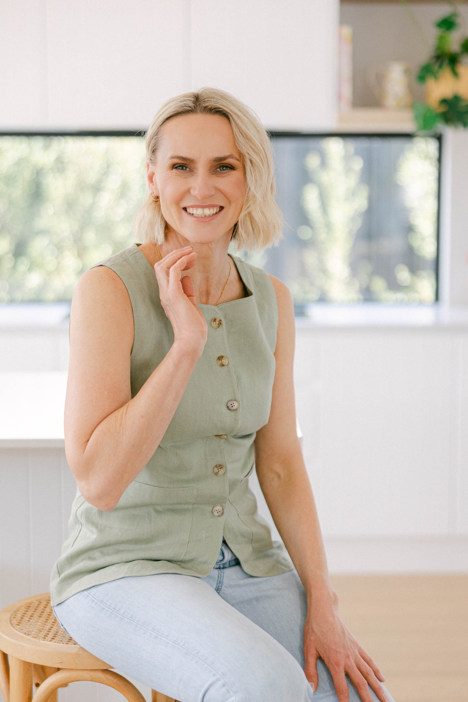 Zelda Green, financial educator for photographers and money mindset coach, smiling at camera in a brightly lit home wearing a blue jeans and a green waistcoat